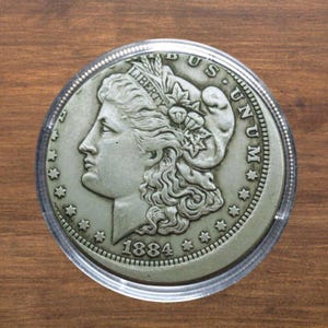May include: A silver coin from 1884, featuring a profile of a woman with flowing hair and the word "LIBERTY". The coin is encased in a clear plastic holder. The words "E PLURIBUS UNUM" are visible.
