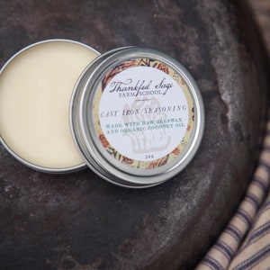 May include: A small tin of cast iron seasoning with a label that reads "Thankful Sage Farm School Cast Iron Seasoning Made with Raw Beeswax and Organic Coconut Oil 2 oz."
