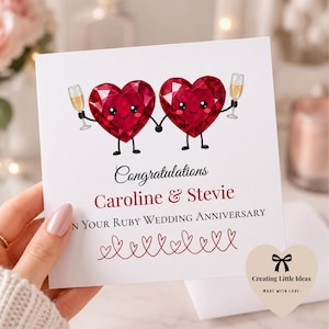 May include: A square greeting card featuring two cartoon ruby heart characters holding hands and champagne flutes. The text reads: Congratulations, Caroline & Stevie, ON YOUR RUBY WEDDING ANNIVERSARY, with a decorative line of small red hearts below.