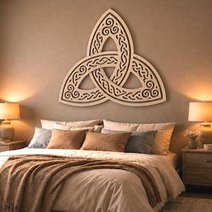 May include: A large, light-coloured wooden wall art piece featuring an intricate, symmetrical triquetra knot design with interlacing patterns and spiral details, mounted centrally on a plain, neutral-toned wall above a bed.