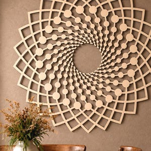 May include: A large, circular wall art piece made of light-colored wood, featuring a geometric pattern of interlocking squares and radiating lines of small circles that spiral toward a hollow center, creating a complex, symmetrical mandala design.