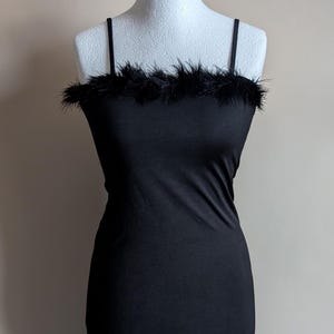 May include: A black dress with a fitted silhouette, featuring delicate spaghetti straps and a feathered edge at the neckline. The dress is presented on a white mannequin. The background is a plain, neutral colour.
