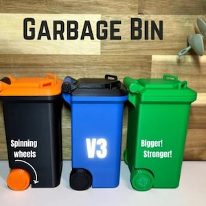 Puede incluir: Tres mini cubos de basura en negro, azul y verde, cada uno con una tapa de diferente color. El cubo negro tiene ruedas y tapa naranjas, el cubo azul tiene ruedas negras y el texto "V3", y el cubo verde tiene ruedas verdes y el texto "Bigger! Stronger!" El texto "GARBAGE BIN" está arriba.