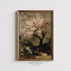 May include: An antique-style framed print of a blossoming tree with pink flowers. The artwork features a detailed depiction of the tree's branches and foliage, set against a muted, cloudy sky. The frame is gold-toned, and the print includes the text "MOSS & INK CO. fine art prints."
