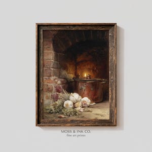 May include: A framed still life print featuring a copper pot, garlic, and herbs in front of a brick fireplace. A small flame flickers inside the pot. The print is labeled "MOSS & INK CO. fine art prints."