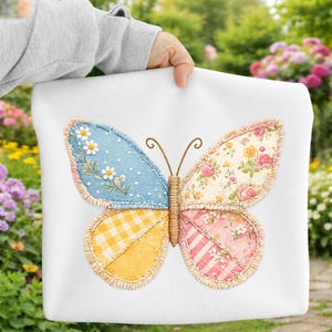 Peut inclure: Coussin blanc avec un grand motif de papillon. Les ailes du papillon sont divisées en quatre sections avec différents motifs : bleu avec des marguerites blanches, floral, vichy jaune et rayures roses avec des fleurs. Antennes marron.