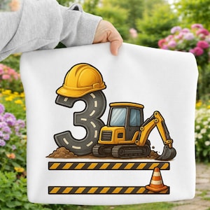 Könnte beinhalten: Weißes Kissen mit einem Baustellenthema. Verfügt über einen gelben Helm auf einer Zahl 3 aus Asphalt, einen gelben Bagger und einen Verkehrskegel. Schwarz-gelbes Warnband befindet sich am unteren Rand.