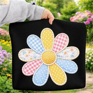 May include: Black pillow with a large, colorful daisy design. The daisy petals are patterned with gingham, polka dots, and floral prints in pastel colors. The center of the flower is yellow, and the petals are outlined with a white border.