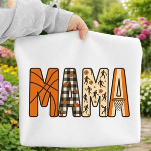 Puede incluir: Bolso de mano blanco con la palabra "MAMA" en naranja, blanco y negro y beige. La letra "M" tiene un diseño de baloncesto, la segunda "A" tiene un patrón de cuadros blancos y negros, la tercera "M" tiene siluetas de jugadores de baloncesto y la última "A" tiene una canasta de baloncesto.