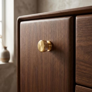 Könnte beinhalten: Nahaufnahme eines Holzschranks mit einem Messingknauf. Der Schrank besteht aus dunkelbraunem Holz mit glatter Oberfläche. Der Messingknauf ist rund, strukturiert und goldfarben. Der Schrank hat ein modernes Design.