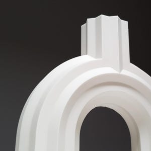 A close-up view of the top section and arch of the white ribbed geometric vase.
