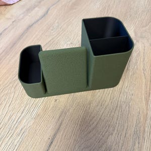A textured, olive green desk organizer with black compartments is shown from a slight angle on a light wood surface.