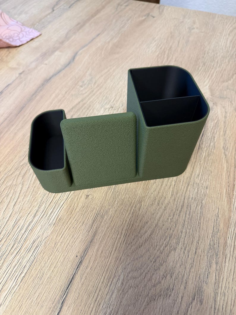 A textured, olive green desk organizer with black compartments is shown from a slight angle on a light wood surface.