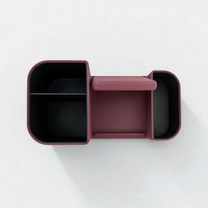 An overhead shot of a dark pink desk organizer with black compartments, showing its three sections and phone stand.