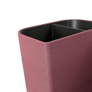A close-up, angled view of the textured surface of a dark pink desk organizer with a black compartment visible inside.