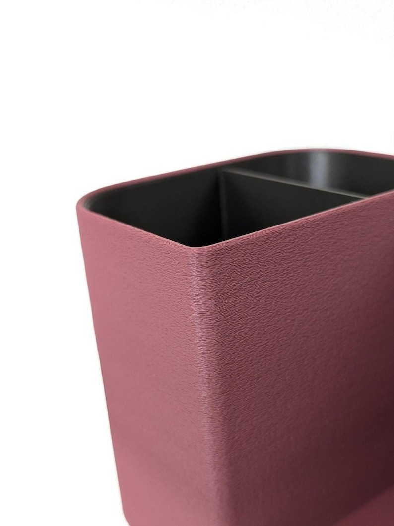 A close-up, angled view of the textured surface of a dark pink desk organizer with a black compartment visible inside.