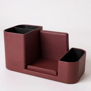 A textured, dark rose-colored desk organizer with black interior compartments, viewed from a slight angle on a light gray surface.