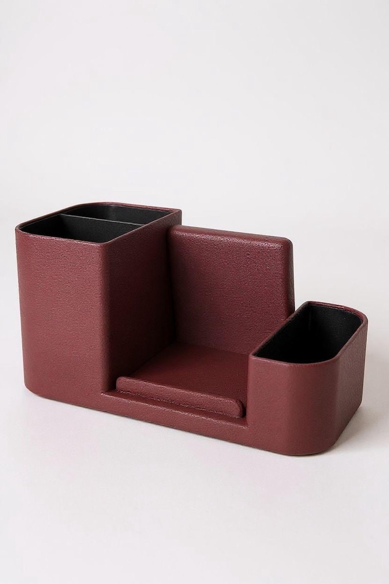 A textured, dark rose-colored desk organizer with black interior compartments, viewed from a slight angle on a light gray surface.