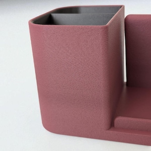 A close-up, angled view of the textured surface of a dark rose-colored desk organizer with a black interior compartment.