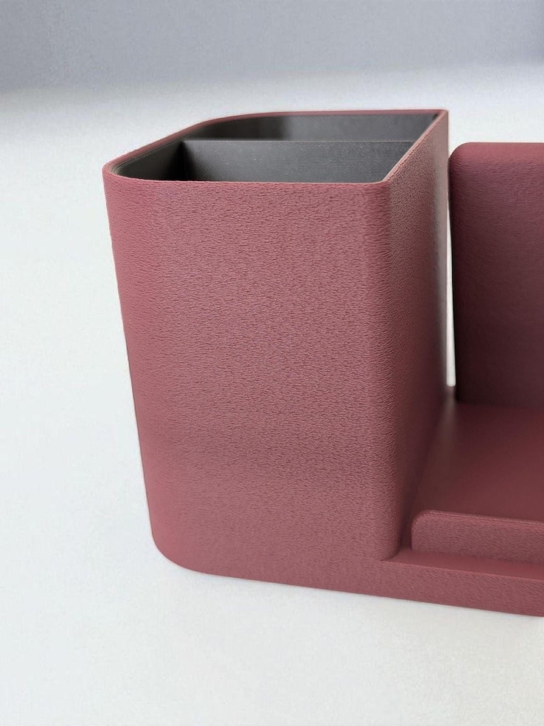 A close-up, angled view of the textured surface of a dark rose-colored desk organizer with a black interior compartment.