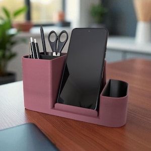 A textured, dark rose-colored desk organizer with a smartphone, black pen, and scissors in its compartments, on a wooden desk.