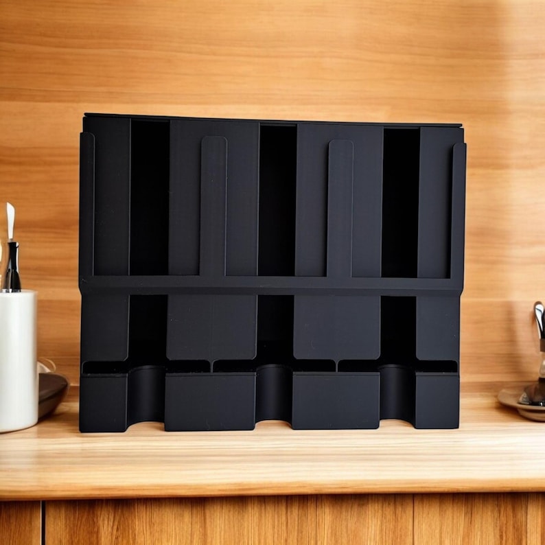 May include: A black organizer with multiple compartments, designed for kitchen or office use. The organizer has a rectangular shape with vertical slots and lower cubby spaces. It is made of a matte black material and sits on a wooden surface.