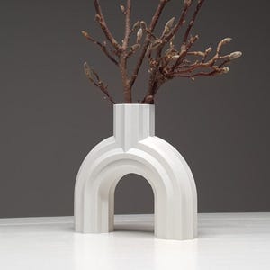 A matte white architectural ribbed arch vase holding bare twigs with buds against a dark grey background.