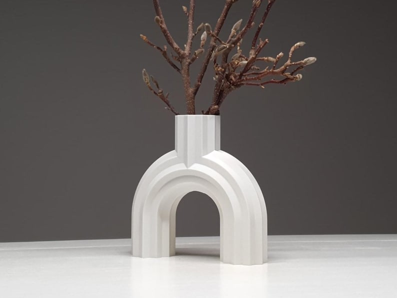 A matte white architectural ribbed arch vase holding bare twigs with buds against a dark grey background.