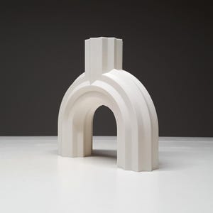 A three-quarter angle view of the white arched ribbed vase on a white table against a dark grey backdrop.