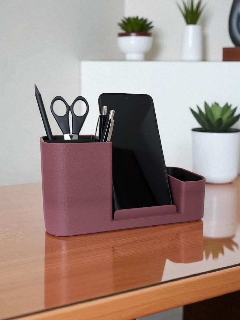 A textured, dark rose-colored desk organizer with a smartphone, black pen, and scissors in its compartments, on a wooden desk.