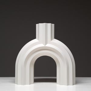 A front-facing view of a white geometric arched vase with vertical ridges standing on a white surface.