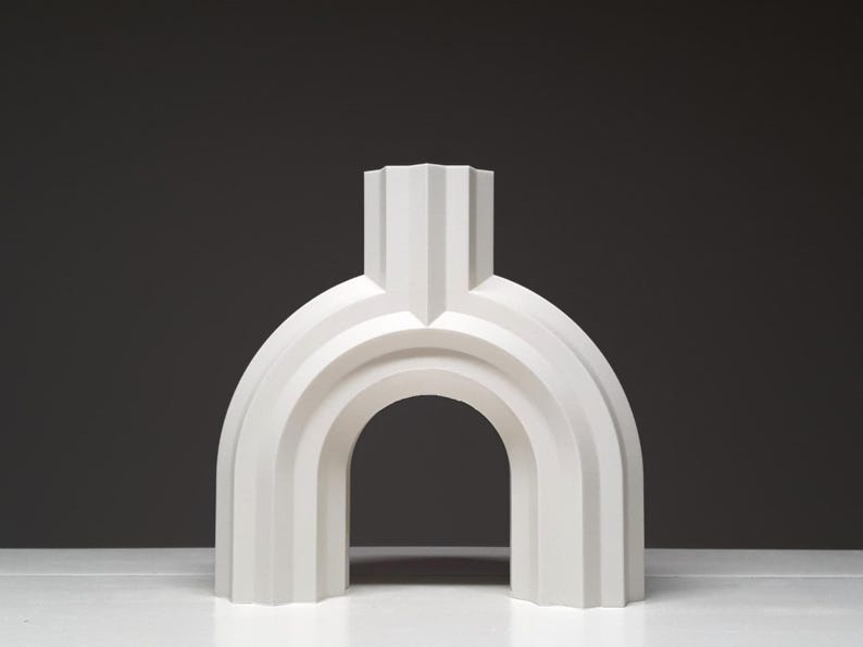 A front-facing view of a white geometric arched vase with vertical ridges standing on a white surface.