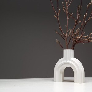 A wide-angle shot of a white ribbed arched vase with branches on a white surface against a dark grey wall.