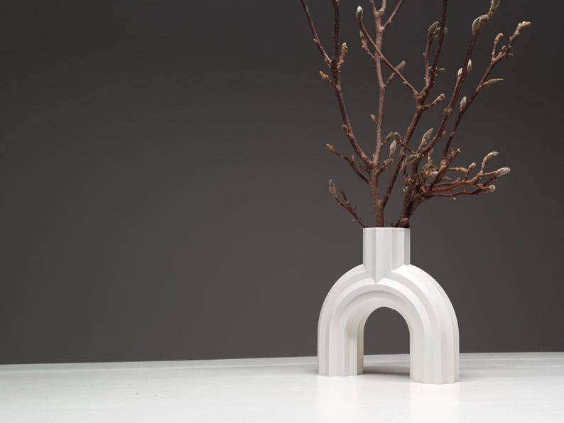 A wide-angle shot of a white ribbed arched vase with branches on a white surface against a dark grey wall.