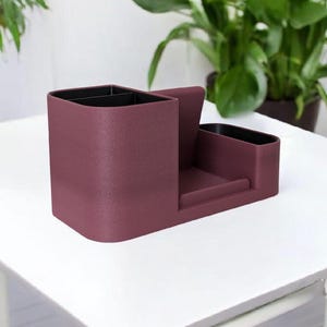 A textured, dark rose-colored desk organizer with black interior compartments, shown from a side angle on a white table.