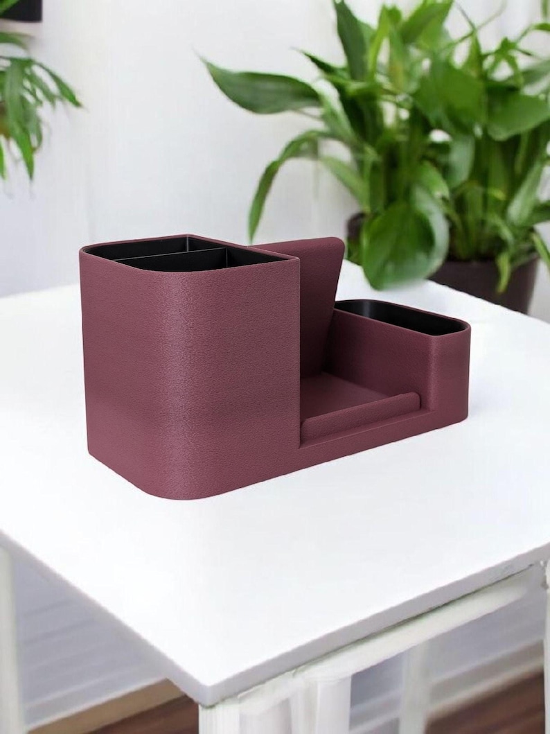 A textured, dark rose-colored desk organizer with black interior compartments, shown from a side angle on a white table.
