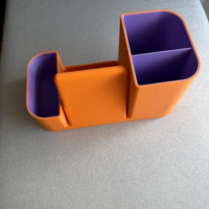 An orange desk organizer with purple compartments is shown from a slight angle on a gray surface.