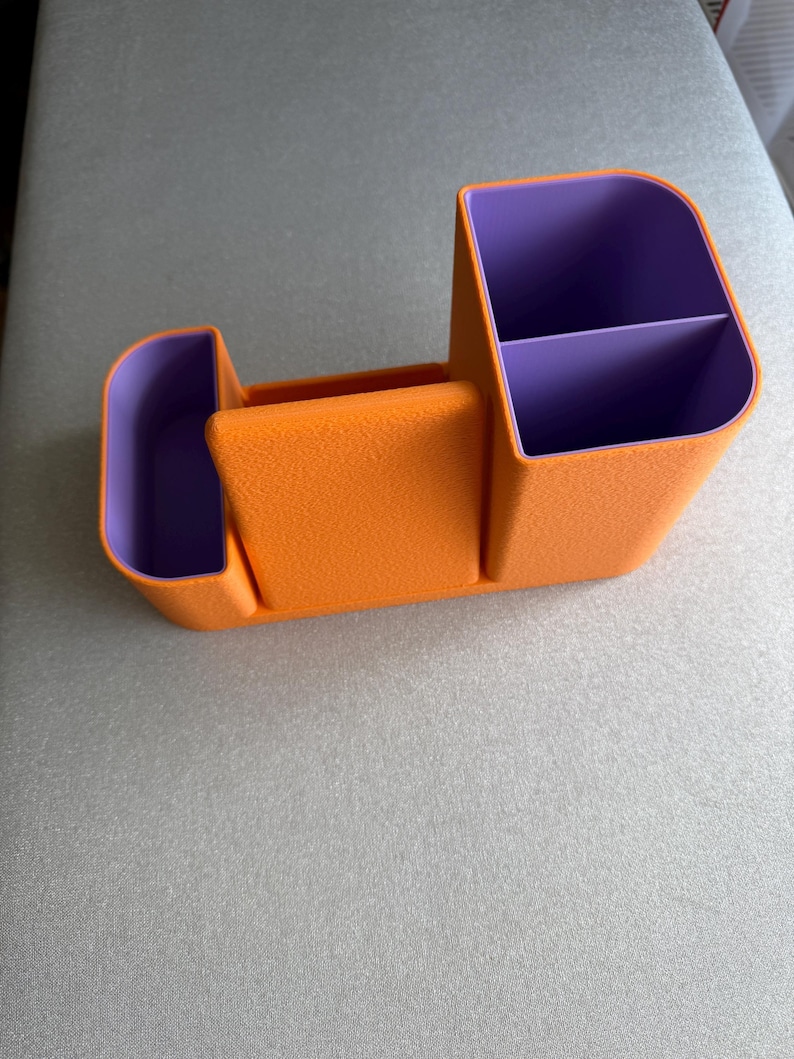An orange desk organizer with purple compartments is shown from a slight angle on a gray surface.