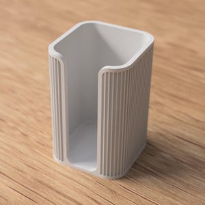 May include: A light gray, rectangular holder with a curved top and vertical ridged sides. The open interior is visible, and the holder sits on a wooden surface. The design is minimalist and modern, suitable for various organizational purposes.