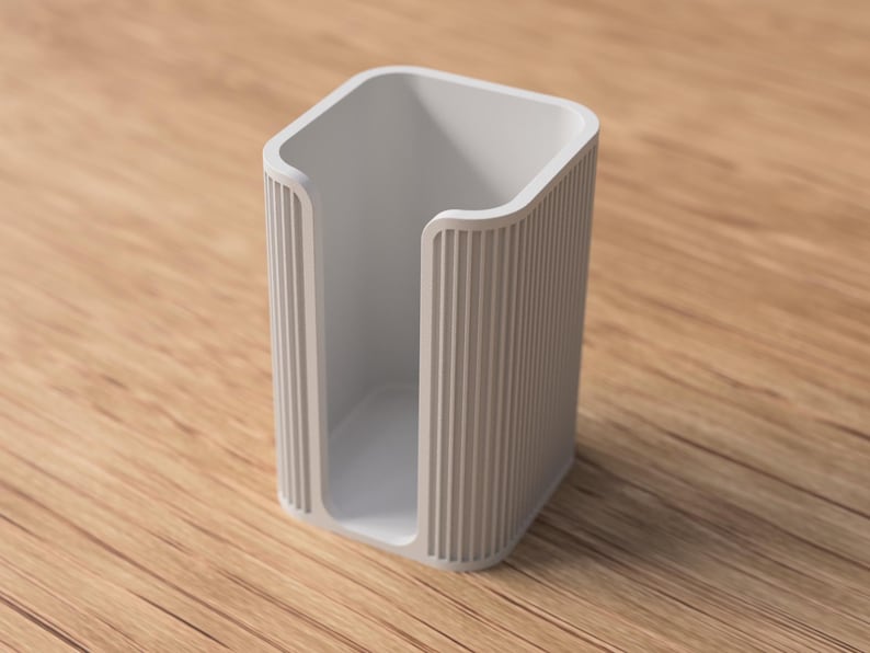 May include: A light gray, rectangular holder with a curved top and vertical ridged sides. The open interior is visible, and the holder sits on a wooden surface. The design is minimalist and modern, suitable for various organizational purposes.