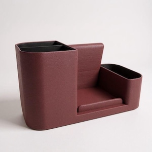 A textured, dark rose-colored desk organizer with black interior compartments, viewed from a side angle on a light gray surface.