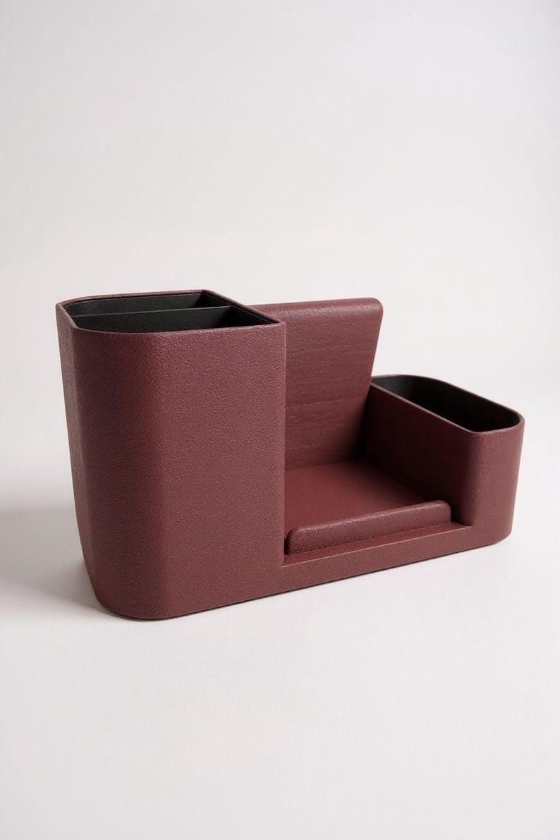 A textured, dark rose-colored desk organizer with black interior compartments, viewed from a side angle on a light gray surface.