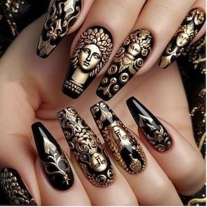 May include: A hand displays a set of long, black, coffin-shaped artificial nails. Each nail features intricate gold designs, including ornate patterns and classical figures. The nails have a glossy finish, creating a luxurious and artistic aesthetic.