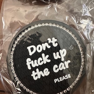 May include: Black car coaster with a textured surface and a rhinestone border. The text "Don't f*ck up the car PLEASE" is in white. The coaster is packaged in clear plastic.