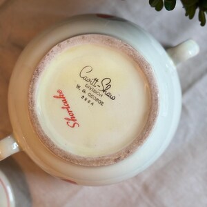 Peut inclure: Le dessous d'un bol en c&eacute;ramique blanche portant l'inscription imprim&eacute;e en noir Cavitt-Shaw Division W. S. George 392 A et le texte en cursive rouge Shortcake. Le bol poss&egrave;de deux anses lat&eacute;rales et une base circulaire avec un bord non &eacute;maill&eacute;.