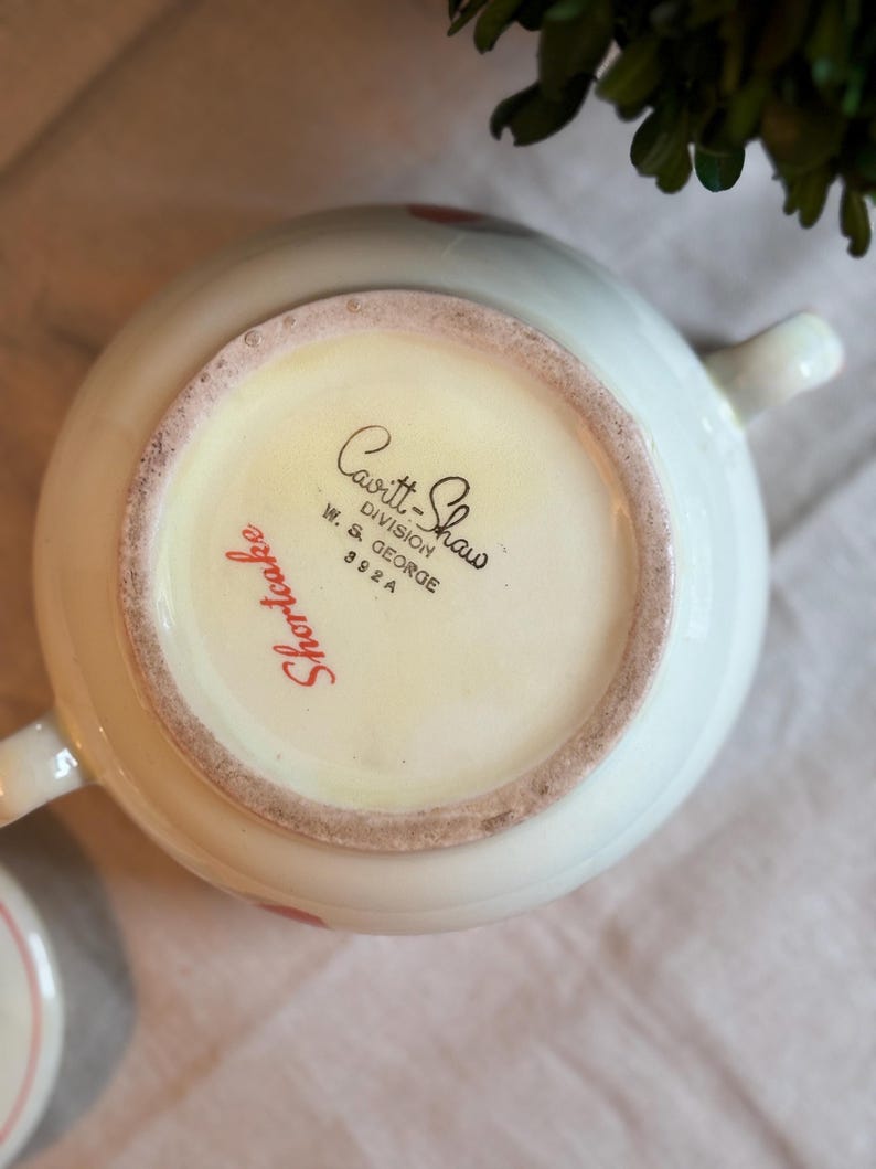 Peut inclure: Le dessous d'un bol en c&eacute;ramique blanche portant l'inscription imprim&eacute;e en noir Cavitt-Shaw Division W. S. George 392 A et le texte en cursive rouge Shortcake. Le bol poss&egrave;de deux anses lat&eacute;rales et une base circulaire avec un bord non &eacute;maill&eacute;.