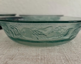 May include: A set of clear, teal-colored glass bowls. Each bowl features a detailed embossed fruit design around the rim. The bowls have a rounded shape and are suitable for serving various dishes.