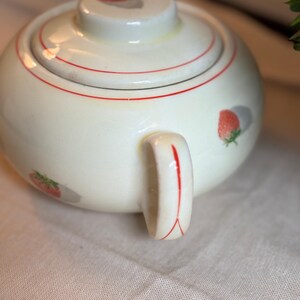 Peut inclure: Un sucrier rond en c&eacute;ramique de couleur cr&egrave;me avec un couvercle assorti. L'objet pr&eacute;sente un motif d&eacute;licat de petites fraises rouges avec des feuilles vertes et de fines lignes rouges circulaires autour du couvercle et de l'anse.