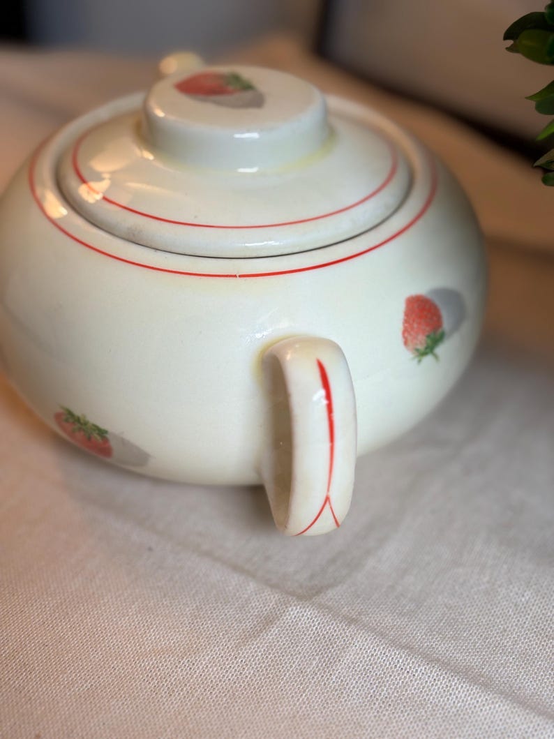 Peut inclure: Un sucrier rond en c&eacute;ramique de couleur cr&egrave;me avec un couvercle assorti. L'objet pr&eacute;sente un motif d&eacute;licat de petites fraises rouges avec des feuilles vertes et de fines lignes rouges circulaires autour du couvercle et de l'anse.