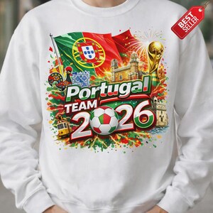 K&ouml;nnte beinhalten: Wei&szlig;es Sweatshirt mit einem lebendigen Grafikdesign, das die portugiesische Fu&szlig;ballmannschaft feiert. Das Design umfasst die portugiesische Flagge, einen Fu&szlig;ball, den Text "Portugal Team 2026" und eine goldene Troph&auml;e. Ein "Best Seller"-Tag ist sichtbar.